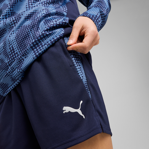 A close-up of a person wearing navy blue Puma training shorts with a visible Puma logo on the left leg.