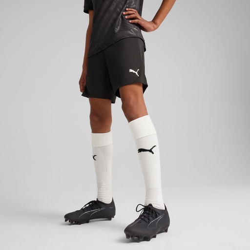 A person wearing Puma Team CUP 25 Shorts in black colour, with a Puma logo on the shorts, standing against a white background.